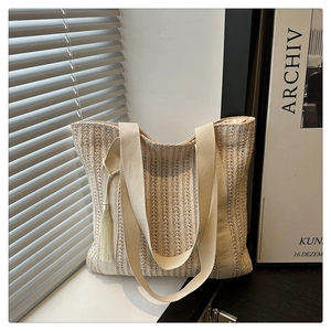 Detail of beige woven straw tote with vertical texture, canvas straps, and side tassel
