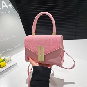 Pink patchwork crossbody bag with woven flap and golden H-shaped buckle on a desk
