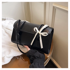 Détail d'un sac baguette noir orné d'un nœud en soie blanche sur double bandoulière