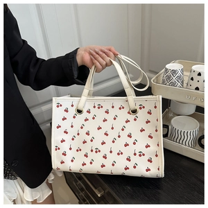 Détail d'un cabas blanc à motifs cerises rouges avec œillets dorés et deux poignées de transport