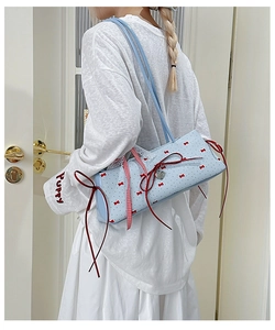 Detail of light blue shoulder bag featuring red bow prints and a heart metal pendant