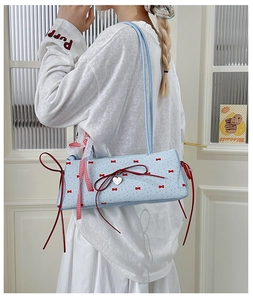 Detail view of light blue baguette bag with red bow prints and heart pendant
