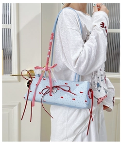 Detail of light blue shoulder bag with red bow prints and a heart metal charm