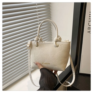 Detail of cream snake-texture handbag with gold FASHION text and knot handles