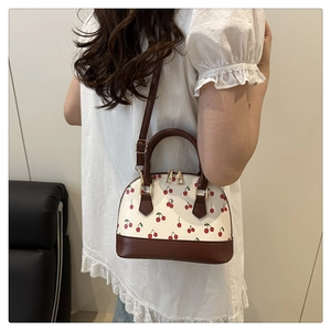 Model view of cream cherry print crossbody bag with brown faux leather trim and gold zipper