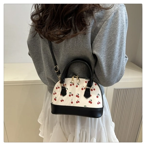 Detailed back view of model wearing a white shell bag with red cherry prints and black strap