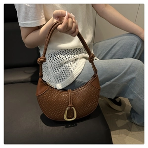 Detail of a brown woven half-moon bag featuring a gold buckle and knotted leather strap