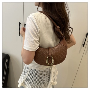 Detail of brown woven leather crescent bag with golden buckle and knotted strap