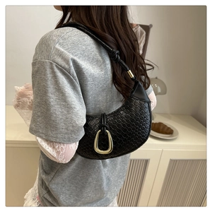 Detail of black woven shoulder bag featuring a knotted strap and gold horseshoe buckle