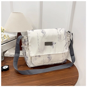 Détail du sac bandoulière blanc avec imprimés papillons et calligraphie sur table en bois