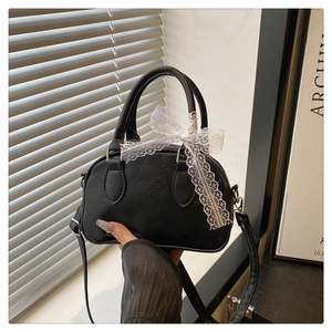 Detail of black Boston bag with embossed patterns and a delicate white lace bow accent
