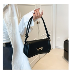 Detail of black leather handbag featuring golden bow clasp and stylish knotted shoulder strap