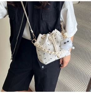Détail du sac seau blanc à cordon avec texture gaufrée et breloque pompon moelleux