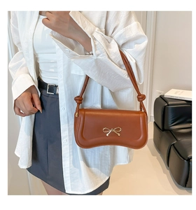 Detail showing the brown leather bag with golden bow buckle and knotted strap