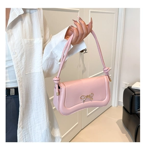 Close-up of pink shoulder bag featuring a golden bow buckle and knotted strap details