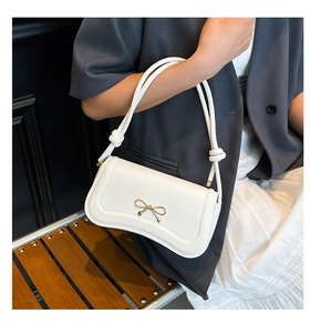 Macro shot of white leather shoulder bag featuring a golden bow buckle and knotted strap