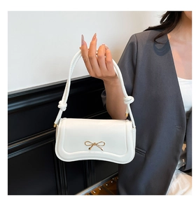 Close-up of a white shoulder bag with a gold metal bow and knotted handle detail