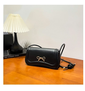 Detail of black leather handbag featuring a golden bow metal charm and knotted strap design