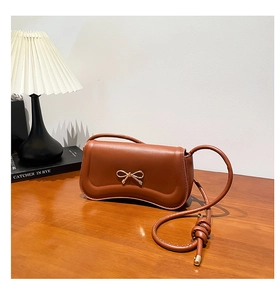 Detail of a brown crescent shoulder bag featuring a golden metal bow and knot strap