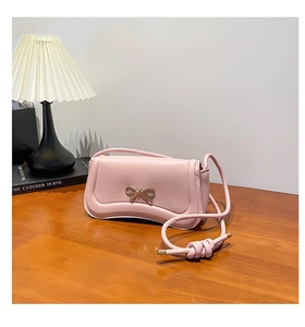 Detailed view of a pink bow shoulder bag with gold hardware on a wooden table
