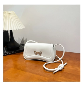 Close-up of white shoulder bag with golden bow hardware and unique wavy bottom edge