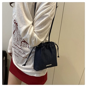 Détail du sac seau en denim bleu foncé avec logo JINGPIN en métal porté par un mannequin