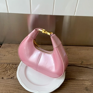 Pink patent leather hobo bag with gold metal buckle detail and half-moon silhouette