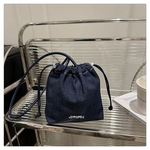Gros plan sur un sac seau en denim bleu avec logo en métal argenté et bandoulière en cuir