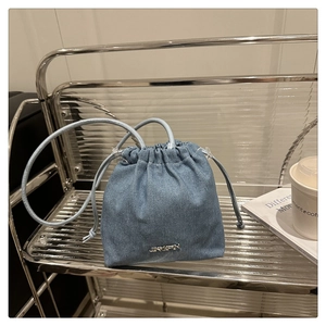Détail du sac seau en jean bleu clair avec fermeture à cordon et logo métallique JINGPIN