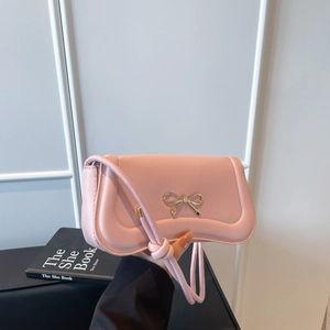Pink crossbody bag with a gold bow buckle, shown by a model against a modern background