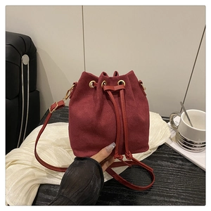 Detail of burgundy suede bucket bag with drawstring closure and golden metal eyelets