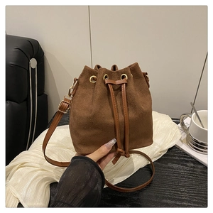 Close-up of brown suede bucket bag featuring drawstring closure and gold metal rings