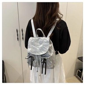 Gros plan du sac à dos en nylon argenté avec broderie NiKa et détails de nœuds noirs