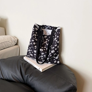 Black canvas tote bag with white floral pattern and lace trim, displayed on a book