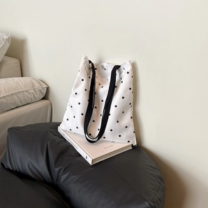 Minimalist white canvas tote bag with black floral print and wide straps on a sofa