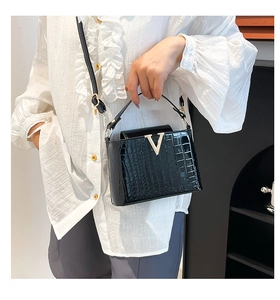 Detail of black crocodile texture bag with gold V-buckle on a white ruffle shirt