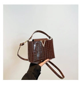 Detail of crocodile pattern texture and golden V-logo on brown bucket handbag
