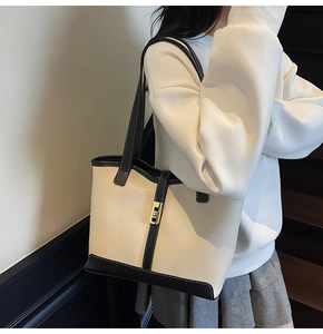 Close-up of a two-tone beige tote bag featuring black trim and a gold twist lock