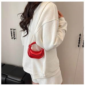 Close-up of shiny red crescent bag with gold chain strap worn as a shoulder bag