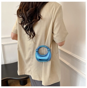 Detail of metallic blue horseshoe-shaped bag with gold chain and round handle