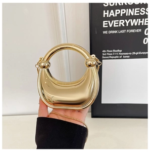 Detail of a crescent-shaped gold metallic handbag with ring handle and a fine chain strap