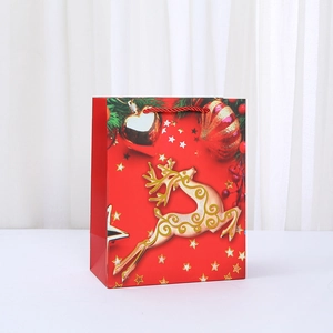 Red Christmas gift bag with golden reindeer prints and woven handles for holiday shopping