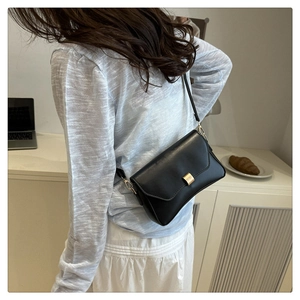Detail einer schwarzen quadratischen Tasche mit goldener Schnalle an einem Modell