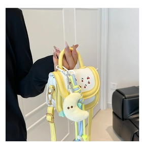 Detail of a mini yellow and beige crossbody bag with cherry prints and moon pendant
