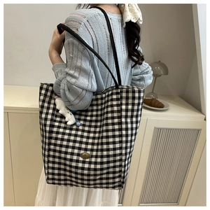 Close-up of black and white checkered tote bag with handmade metal tag and plush charm