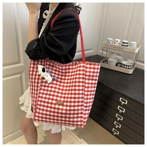 Detail of red checkered canvas tote bag with shoulder strap and plush dog pendant