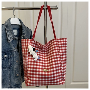 Detail of red checkered canvas tote bag with metal handmade tag and plush dog charm