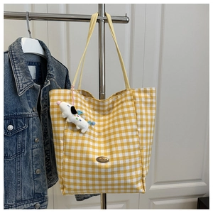 Detail of yellow gingham tote bag with handmade metal tag and plush dog charm accessory