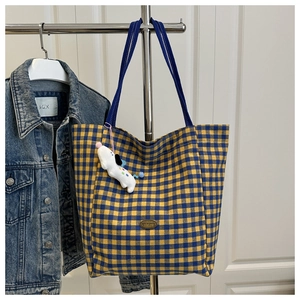 Detail of yellow and blue checkered canvas tote bag with a plush dog charm and metal tag