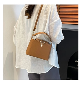 Vue détaillée du logo V doré sur un sac seau marron avec texture en cuir raffiné